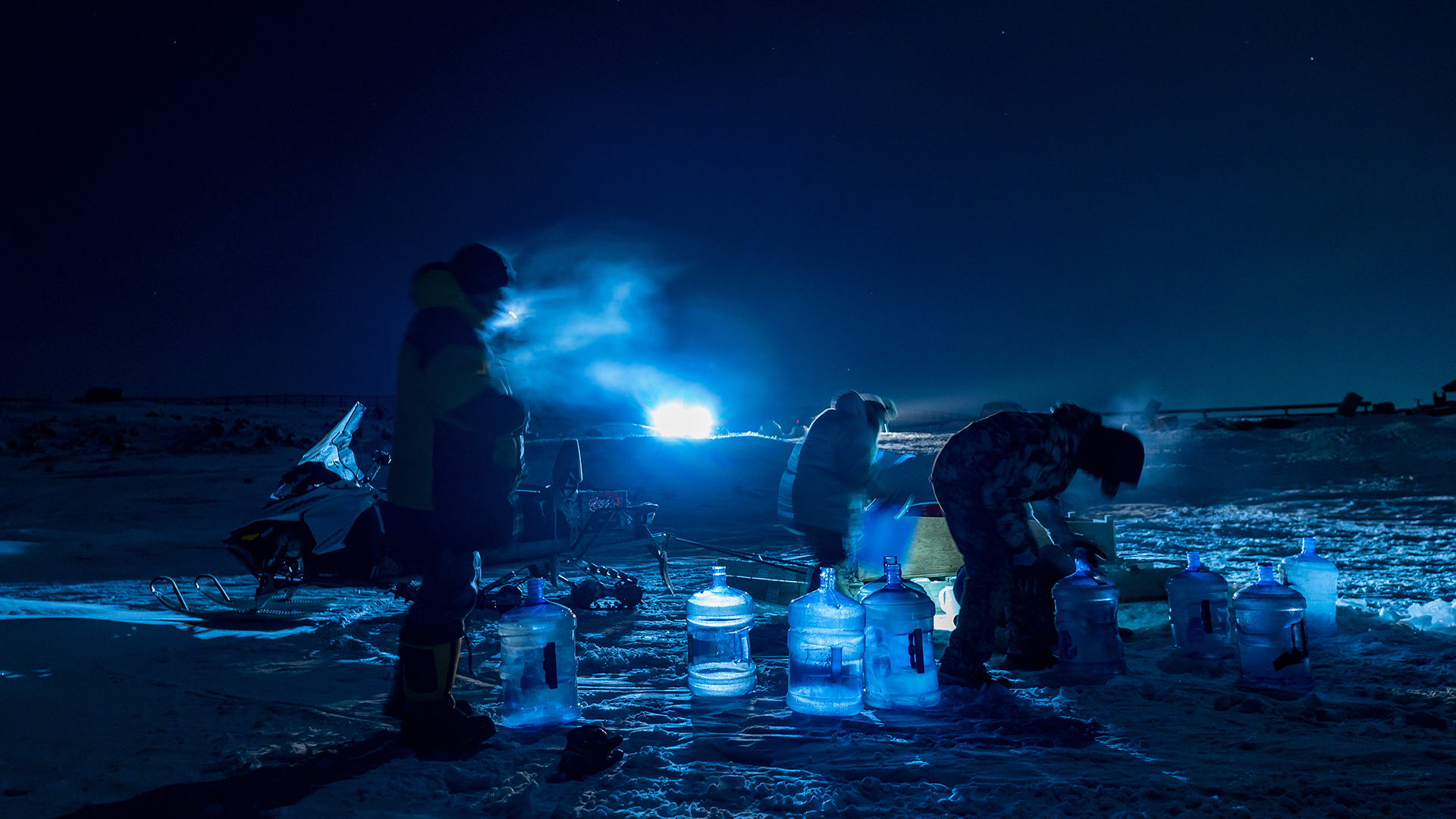 Des résident d'Iqaluit recueillent de l'eau dans une rivière, à travers le couvert de glace. 