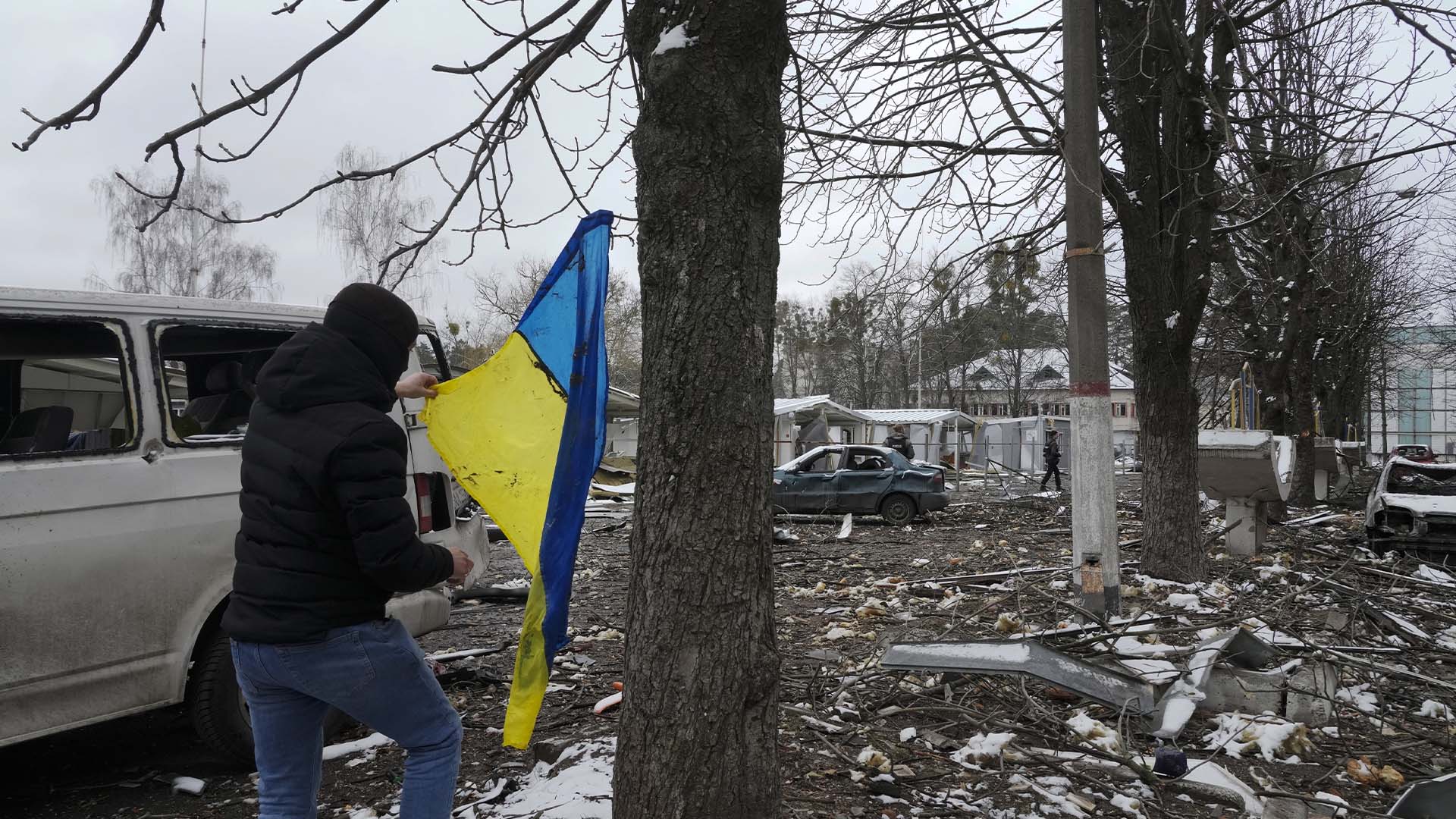 Un homme prend un drapeau national ukrainien suspendu à un arbre alors qu’il marche près d’un bâtiment d’hébergement détruit près d’un poste de contrôle à Brovary, à l’extérieur de Kiev, en Ukraine, le mardi 1er mars 2022.