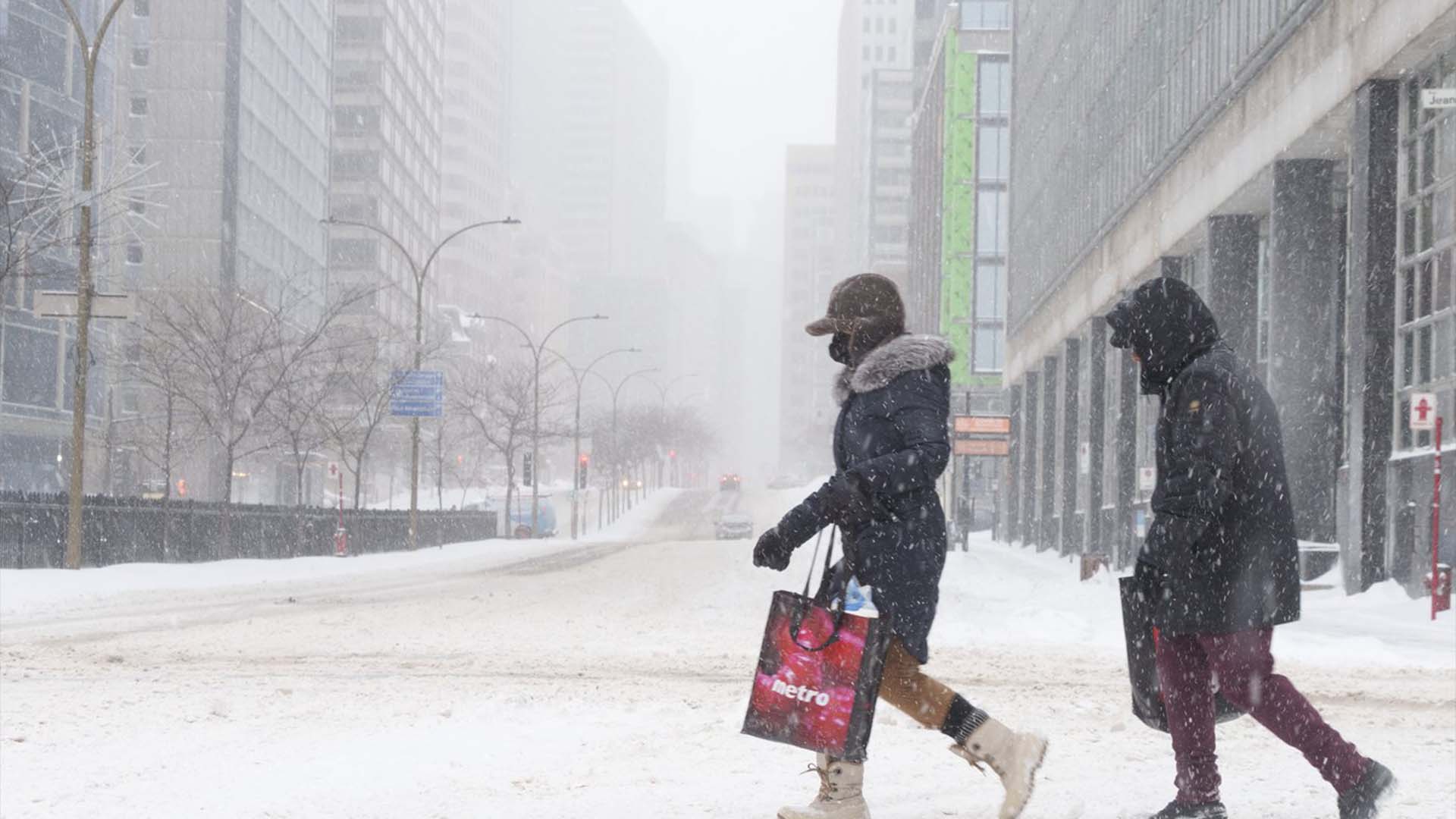 Des piétons traversent une rue presque déserte du centre-ville de Montréal lors d'une tempête de neige hivernale le lundi 17 janvier 2022.