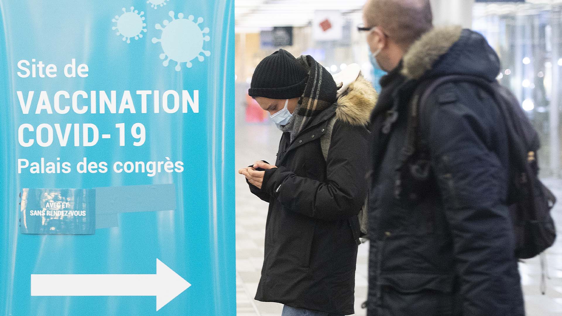 Des gens passent devant un panneau de vaccination contre la COVID-19 sur un site de vaccination à Montréal, le samedi 8 janvier 2022. 