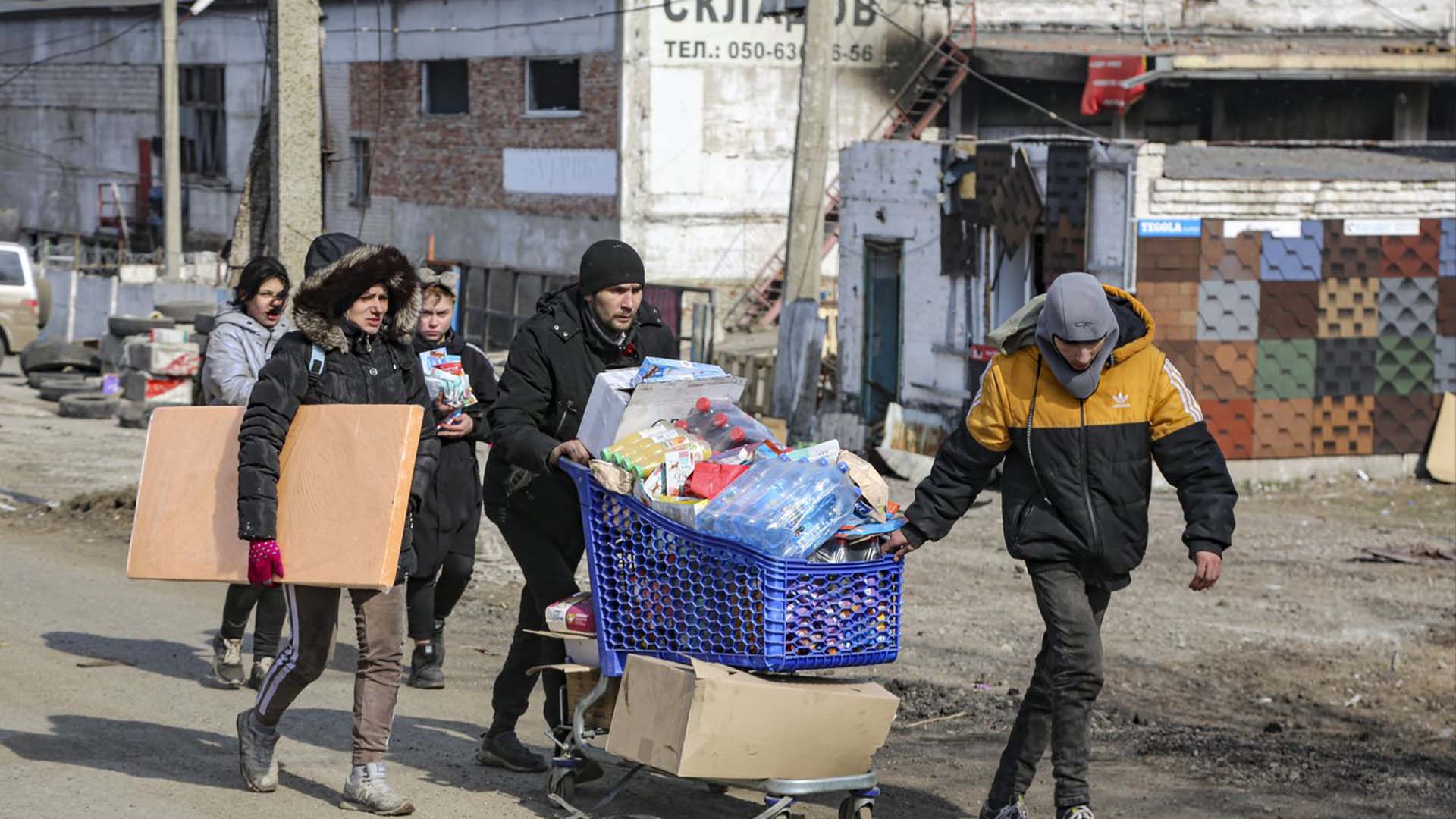 Les résidents locaux transportent de l'eau depuis l'entrepôt alimentaire, sur le territoire sous le contrôle du gouvernement de la République populaire de Donetsk, à la périphérie de Marioupol, en Ukraine, le vendredi 18 mars 2022.