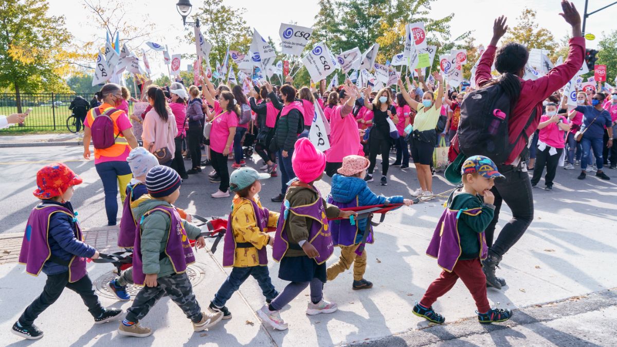 Des enfants d'une garderie passent devant une manifestation de travailleurs de garderie lors du premier jour des grèves tournantes à Montréal, en octobre 2021. 