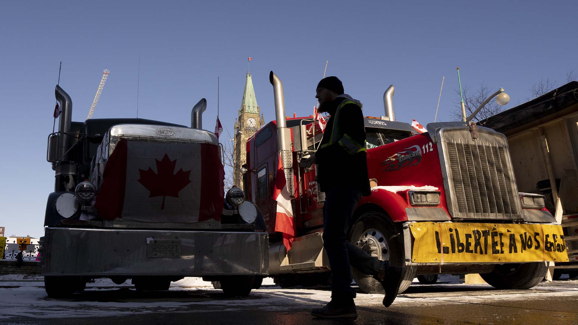 Un homme passe devant des camions garés devant les édifices du Parlement, le mardi 15 février 2022 à Ottawa.