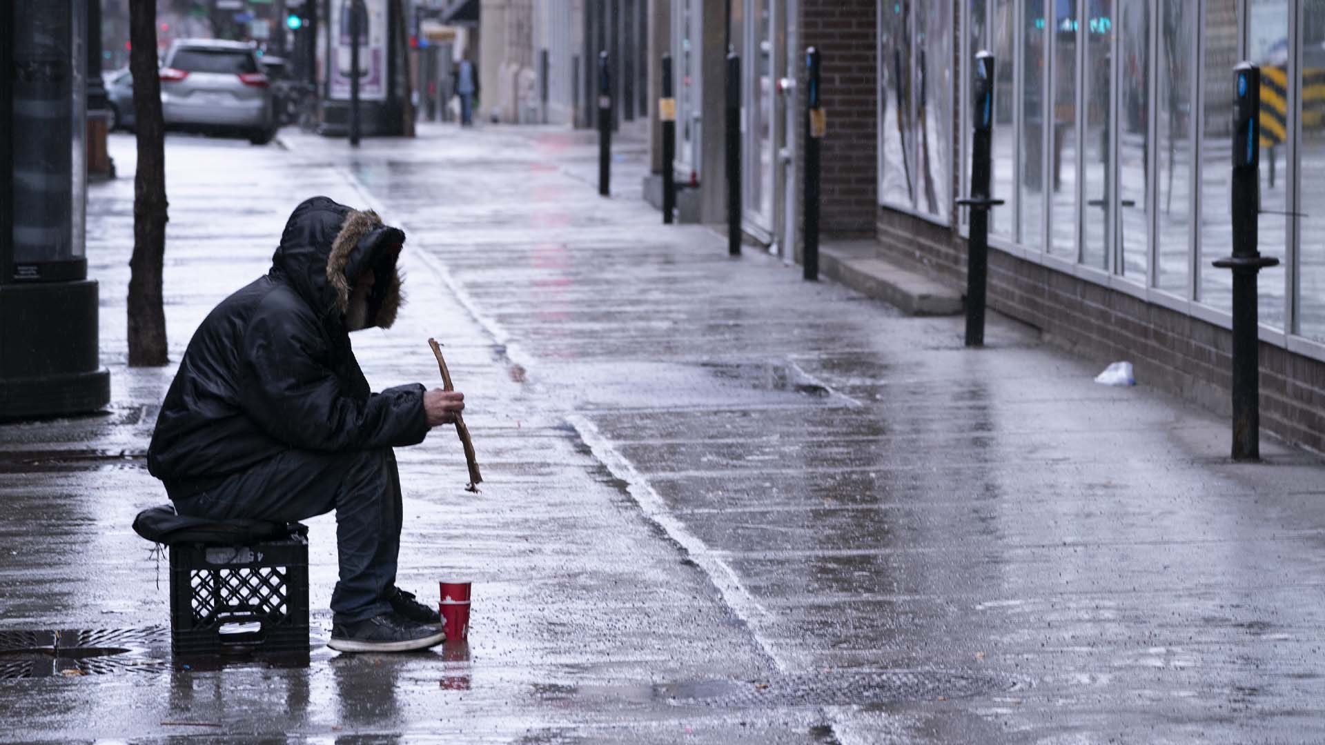 Un sans-abri est assis seul sur un trottoir du centre-ville de Montréal le lundi 30 mars 2020.