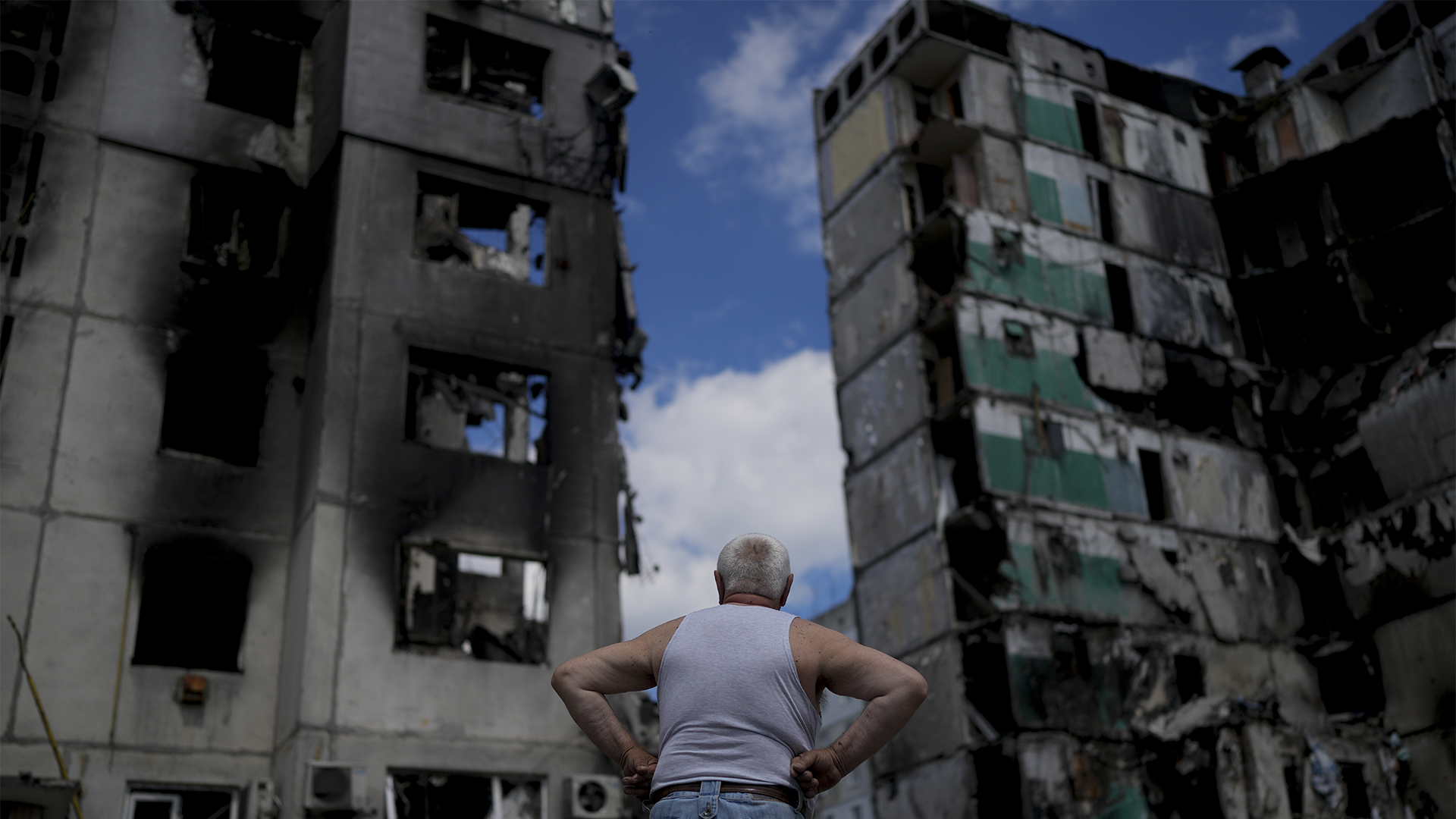 Un homme se tient devant des bâtiments dévastés à 