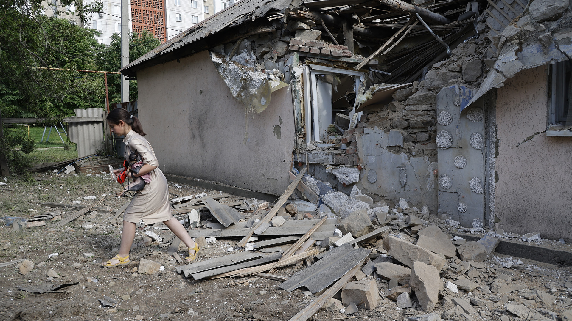 Une fille porte un chien alors qu'elle passe devant une maison endommagée par des bombardements dans le district de Leninsky à Donetsk, sur le territoire sous le contrôle du gouvernement de la République populaire de Donetsk, dans l'est de l'Ukraine, le lundi 6 juin 2022.