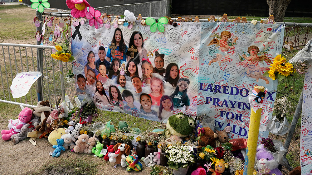 Des peluches sont placés devant une affiche qui comporte les portraits des victimes d'une fusillade dans une école à Uvalde au Texas.