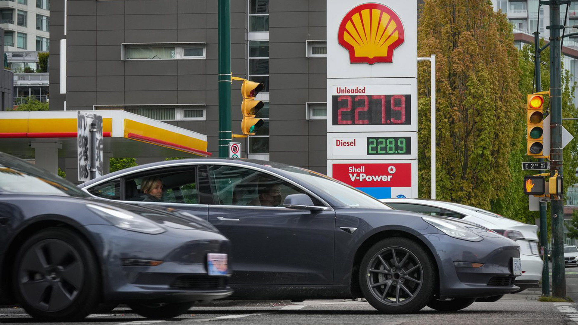 Les véhicules électriques Tesla passent devant un panneau indiquant le prix d'un litre d'essence ordinaire après avoir atteint un nouveau sommet de 2,28 $ à Vancouver le samedi 14 mai 2022.