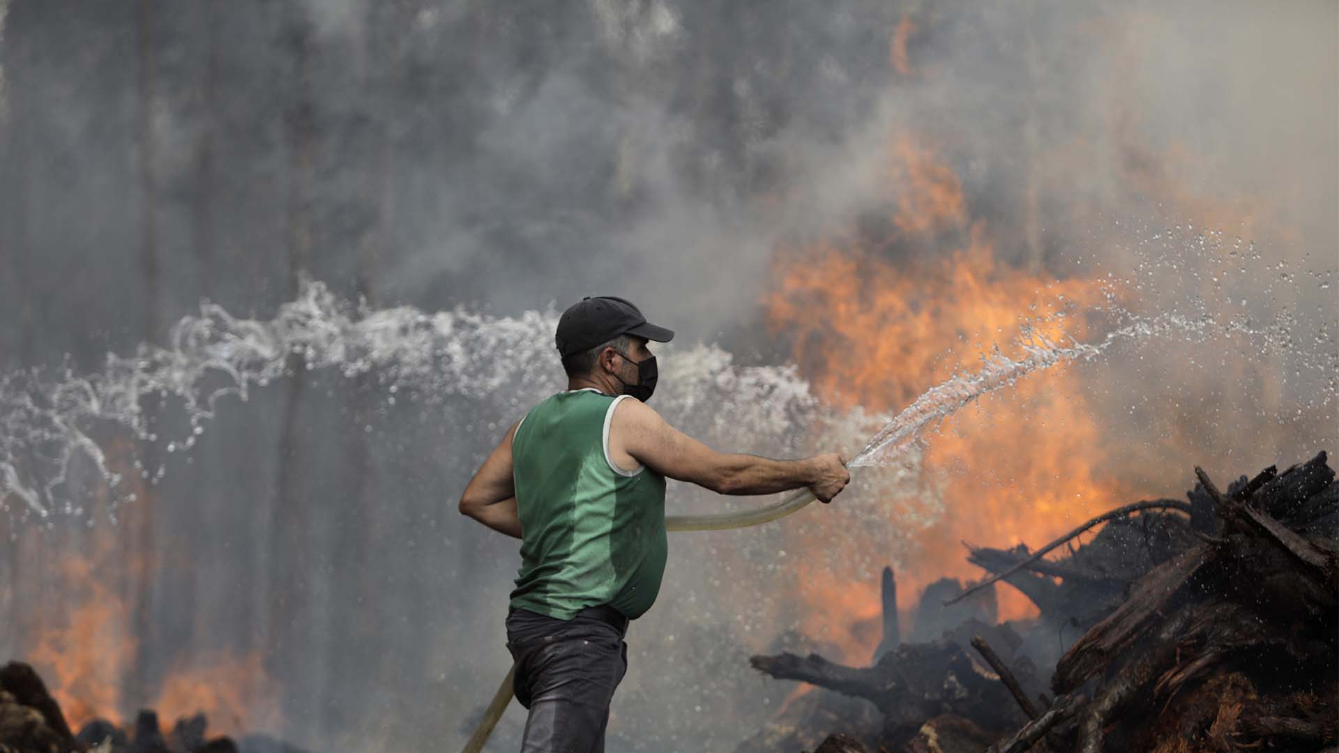 Un résident utilise un tuyau d’arrosage pour tenter d’empêcher un incendie de forêt d’atteindre les maisons du village de Figueiras, à l’extérieur de Leiria, dans le centre du Portugal, le mardi 12 juillet 2022.