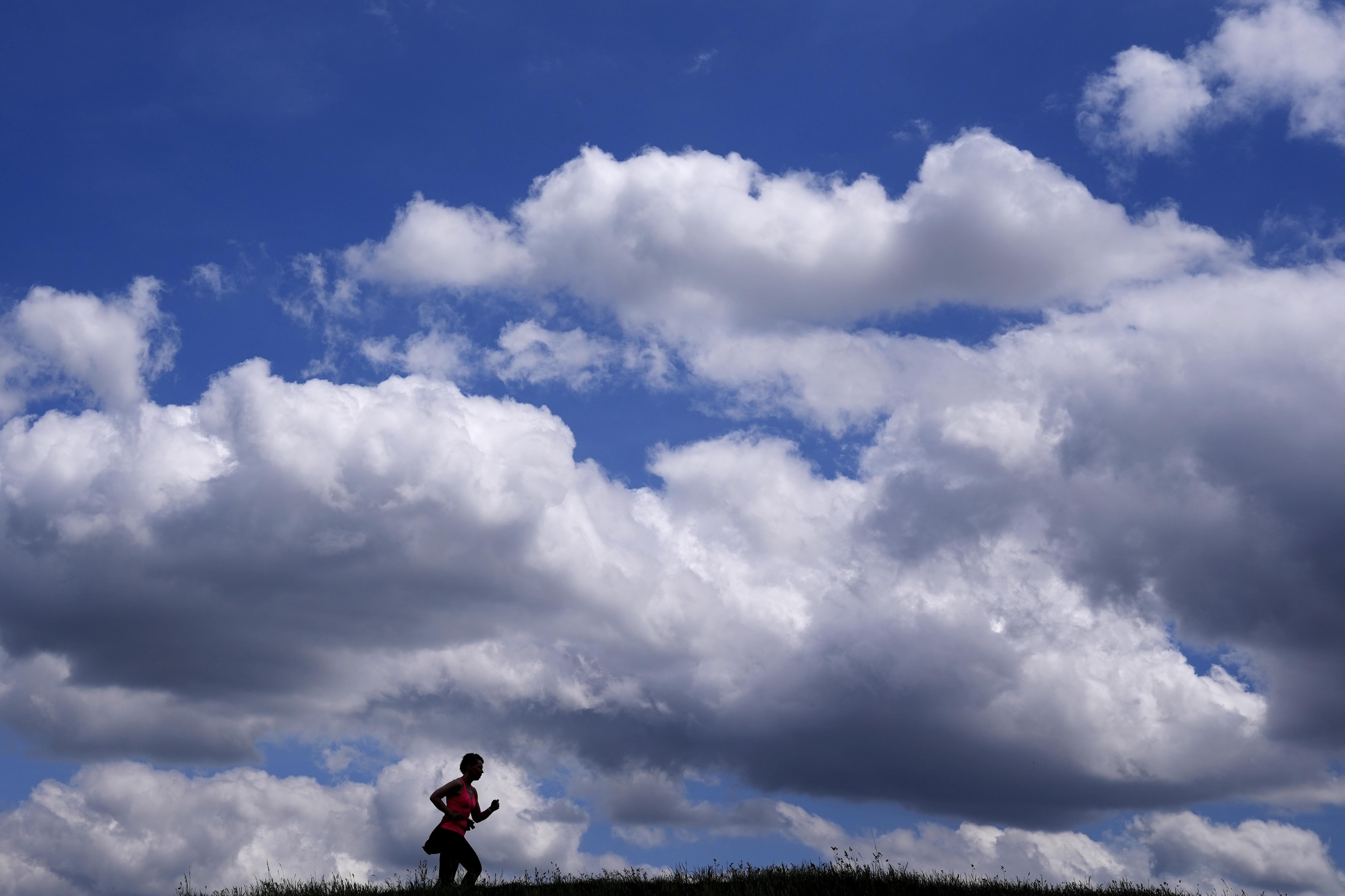 A woman jogs under a cloudy sky in Munich, Germany, Friday, May 27, 2022. (AP Photo/Matthias Schrader)