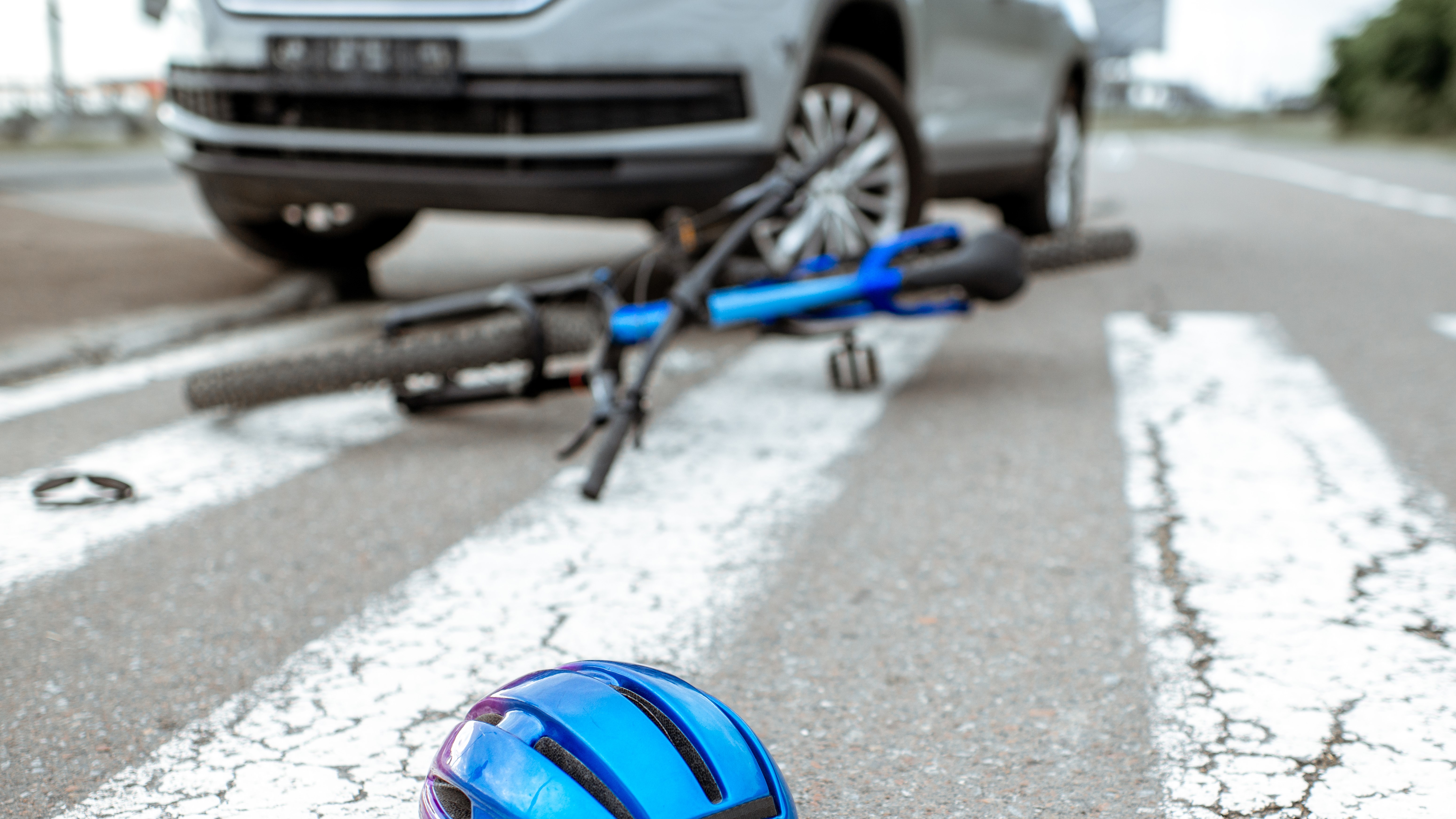 Scene of a road accident with car and broken bicycle lying on the pedestrian crossing. Helmet on the foreground