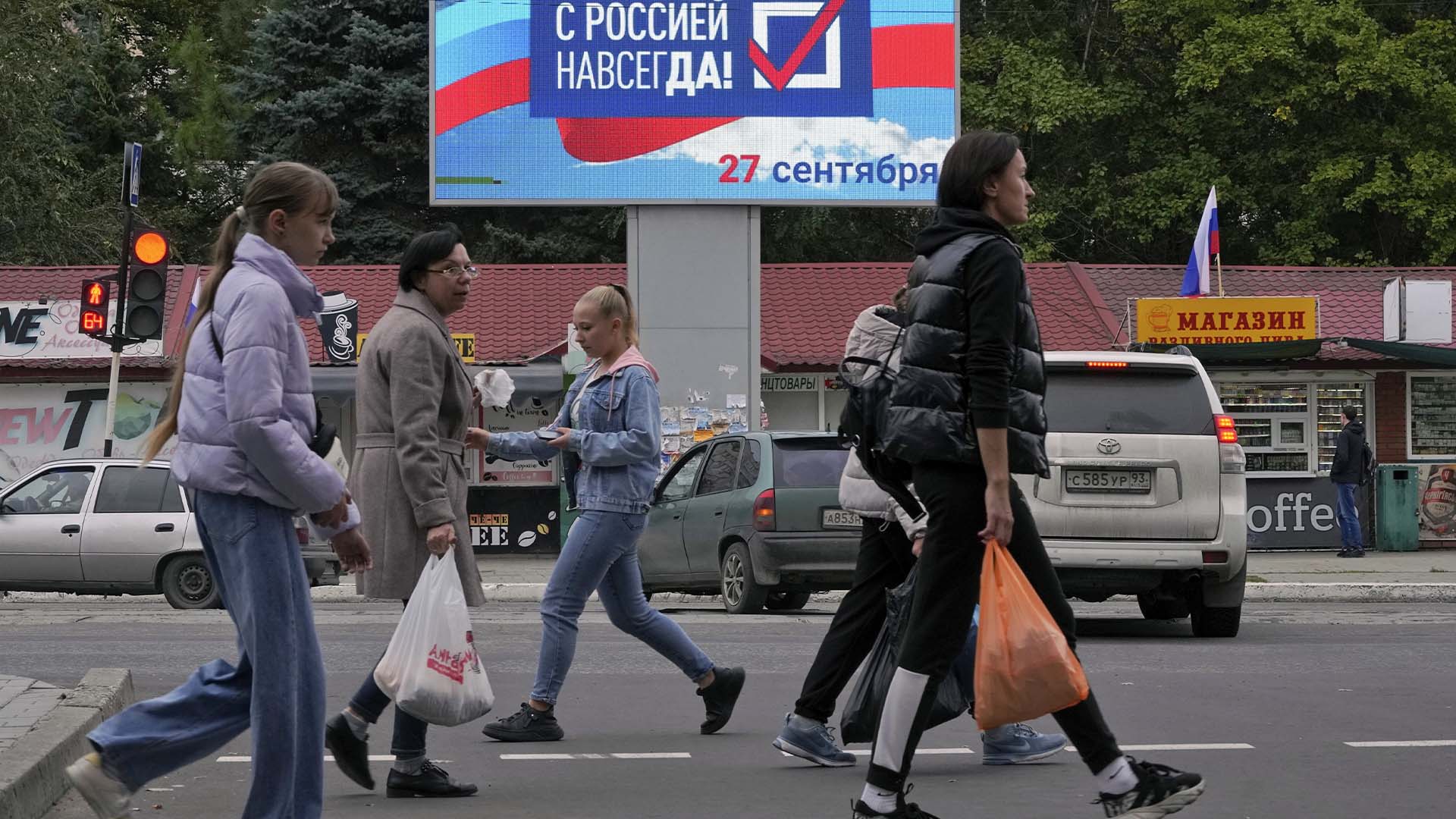 Des gens passent devant un panneau d'affichage indiquant «Pour toujours avec la Russie» à Louhansk, dans la République populaire de Lougansk contrôlée par des séparatistes soutenus par la Russie, dans l'est de l'Ukraine, le mardi 27 septembre 2022.