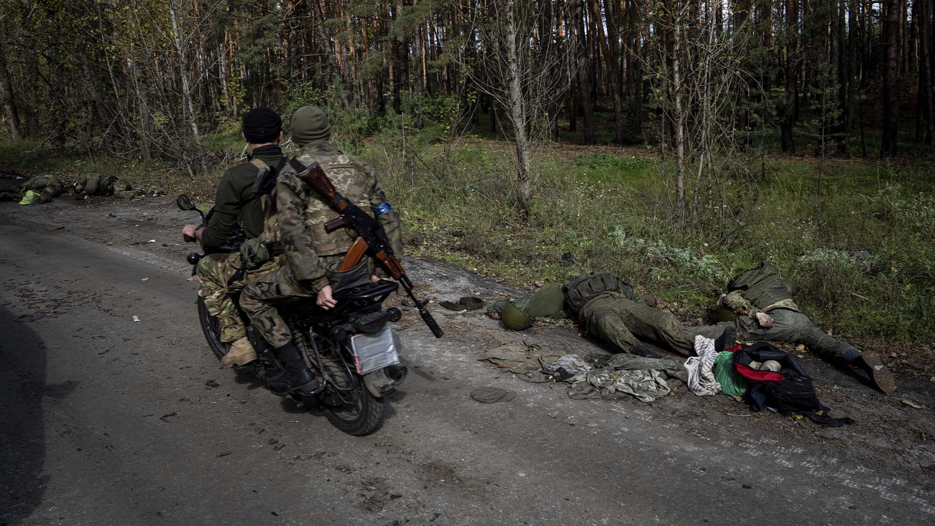 Des militaires ukrainiens conduisent une moto devant les corps d'un militaire russe dans la ville récemment reprise de Lyman, en Ukraine, le lundi 3 octobre 2022.