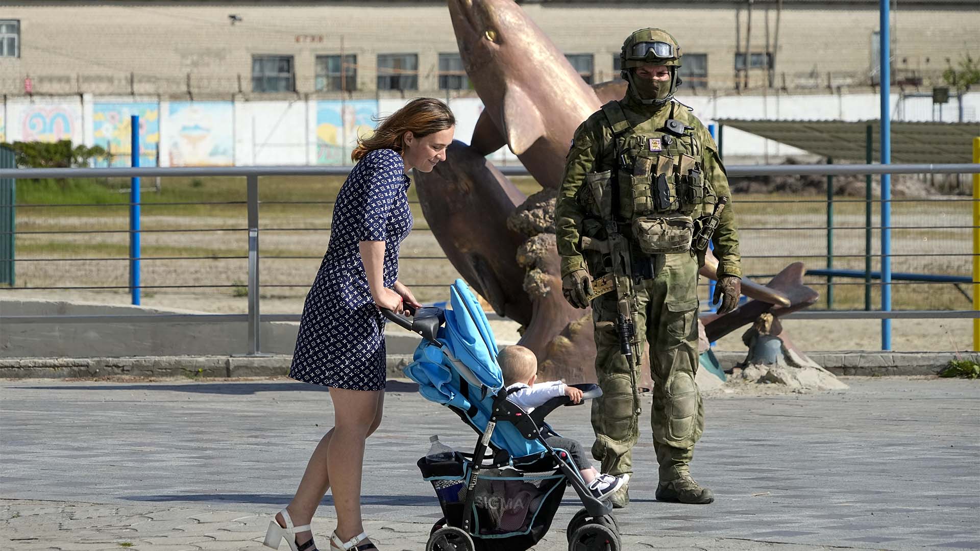 Une femme avec son enfant passe devant un soldat russe sur une digue de la mer Noire à Kherson