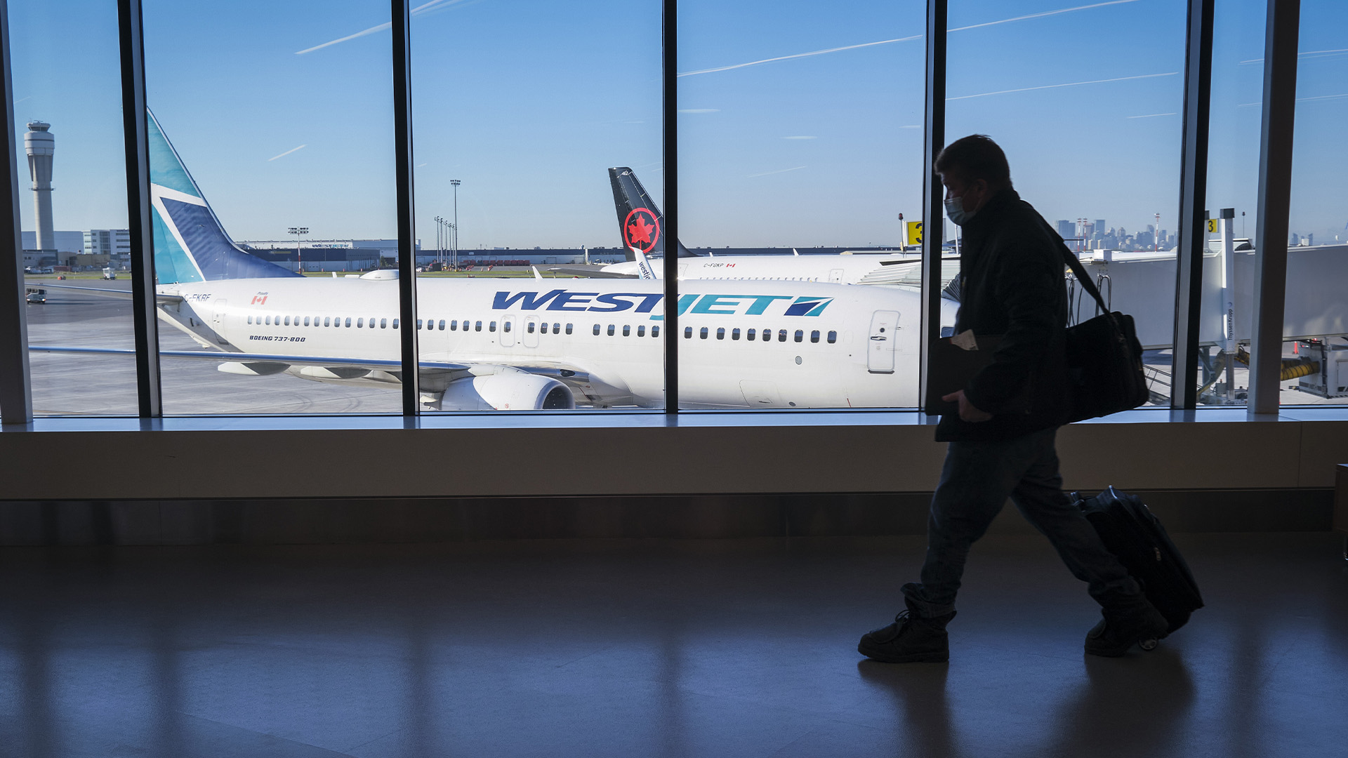 Des passagers passent devant des avions d'Air Canada et de WestJet à l'aéroport international de Calgary à Calgary, en Alberta, le mercredi 31 août 2022.