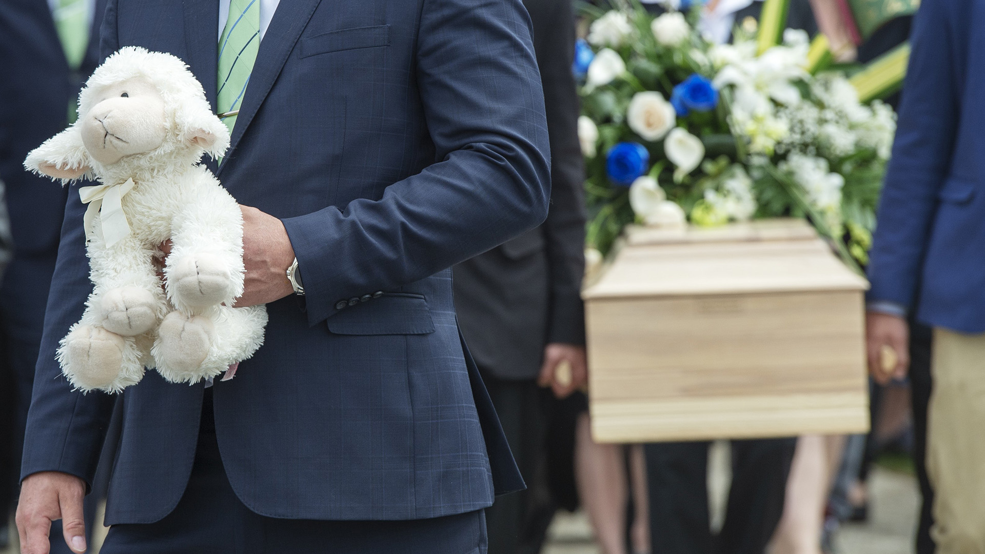 Un homme tient une peluche à proximité du cercueil de la fillette martyre de Granby, lors des funérailles de celle-ci en mai 2019.
