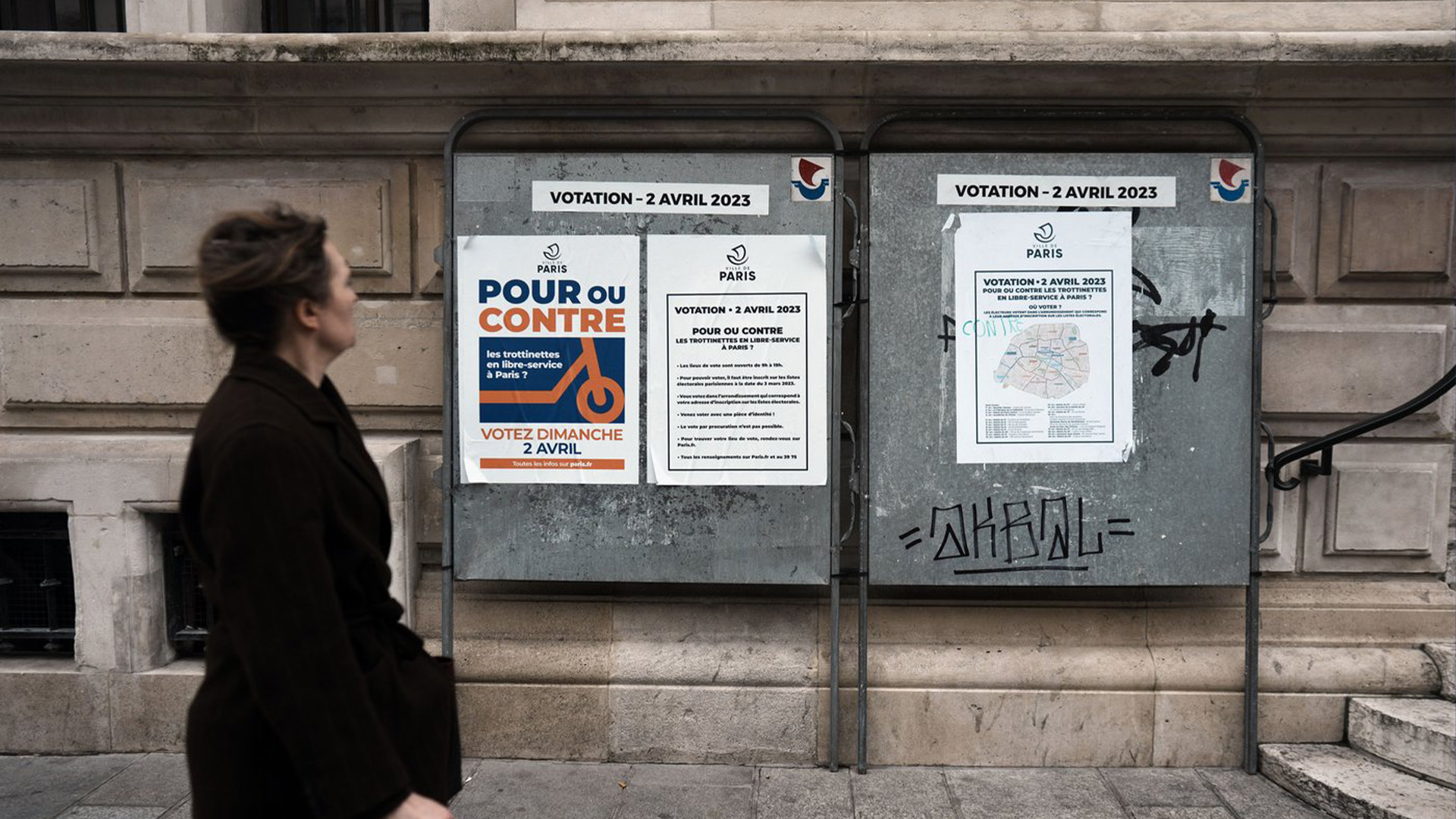 Une femme passe devant une affiche indiquant «Pour ou contre les scooters en libre service à Paris» sur la façade de l'hôtel de ville du 10e arrondissement de Paris, dimanche 2 avril 2023.