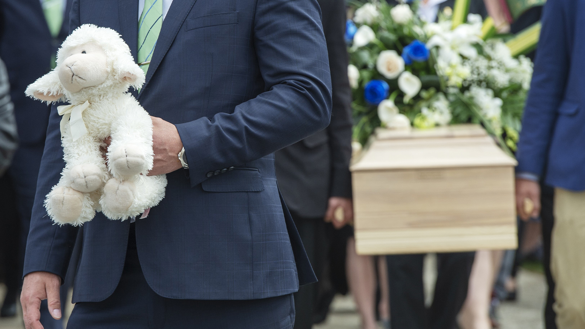 Un homme tient une peluche à proximité du cercueil de la fillette martyre de Granby, lors des funérailles de celle-ci en mai 2019.