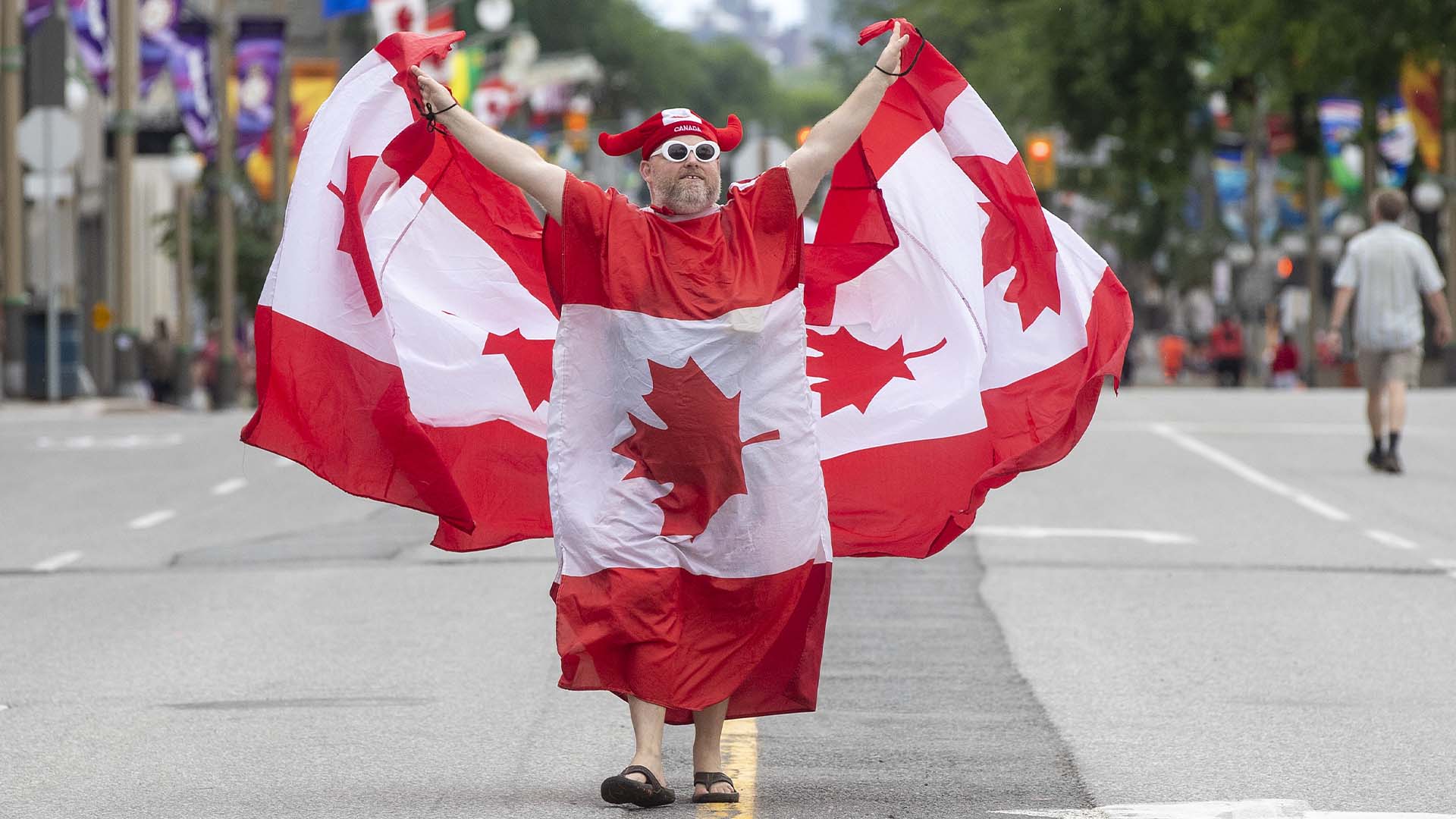 Une personne porte plusieurs drapeaux sur la rue Wellington pendant la fête du Canada à Ottawa, le 1er juillet 2022.