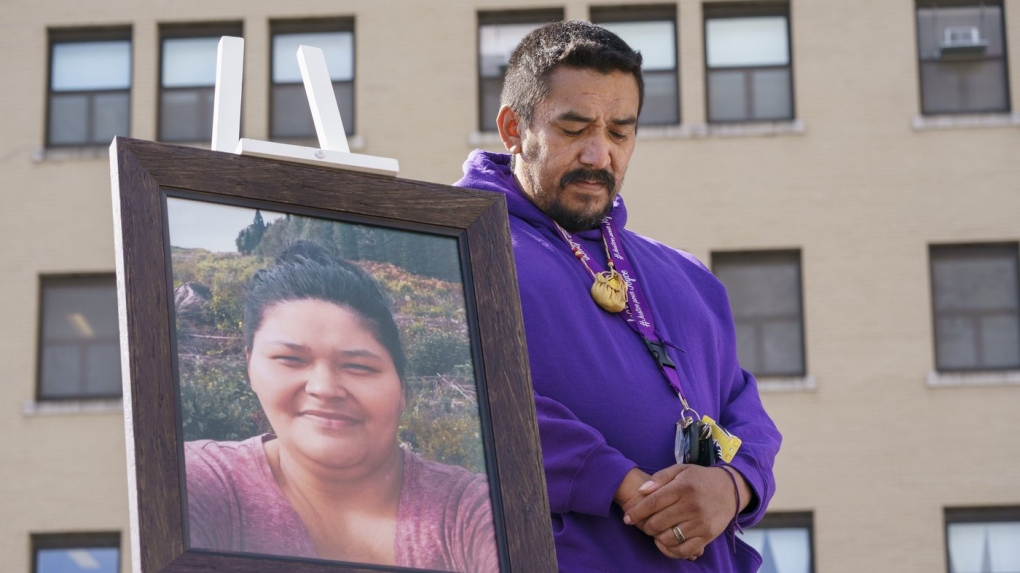 Carol Dubé, le mari de Joyce Echaquan, se tient à côté d'une photo de sa défunte épouse devant l'hôpital où elle est décédée, à Joliette, au Québec, lors d'un mémorial le 28 septembre 2021, marquant le premier anniversaire du décès de sa femme.
