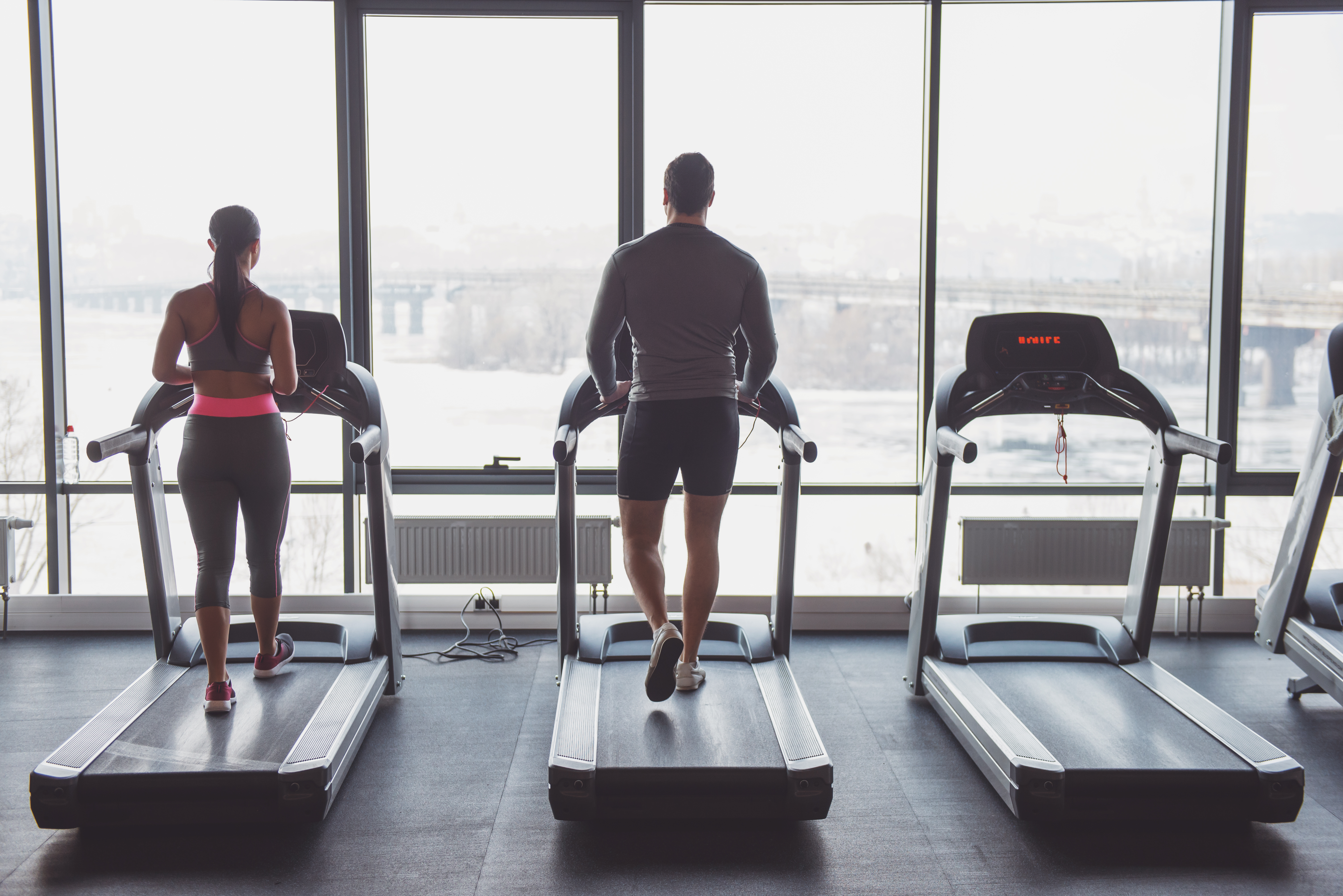 Back view of attractive young muscular man and woman running on a treadmill in gym