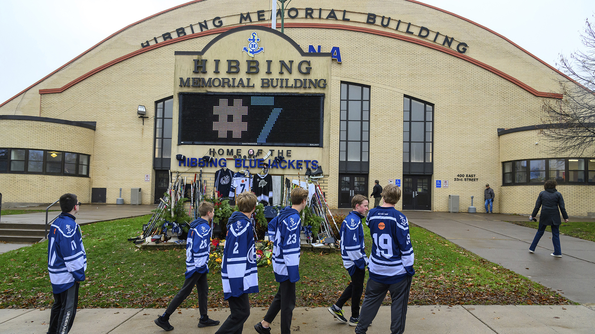 Des membres de l'équipe de hockey de l'école secondaire de Hibbing au Minnesota passent devant le Hibbing Memorial Building le 6 novembre 2023 où a été érigé un hommage à Adam Johnson, décédé après avoir été atteint à la gorge par la lame d'un patin dans un match en Angleterre.