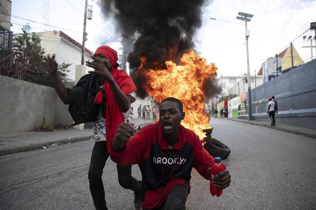 Protesters sing an anti-government song in front of a barricade of burning tires during a protest against the government in Port-au-Prince, Haiti, Friday, Nov. 18, 2022. Canada is sanctioning two of Haiti’s cabinet ministers it accuses of helping violent gangs sow chaos in that country.THE CANADIAN PRESS /AP/Odelyn Joseph