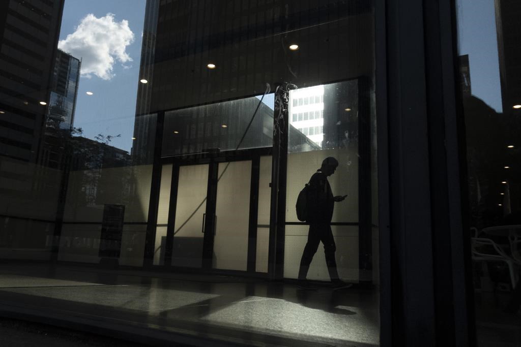 A man walks though a downtown Toronto office building with other buildings reflected in a window in this June 11, 2019 photo. New research suggests a four-day week may be gaining mainstream momentum in corporate Canada as workplaces continue to fine tune post-pandemic schedules and work conditions. THE CANADIAN PRESS/Graeme Roy
