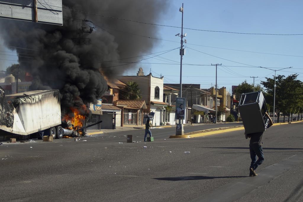Men carry furniture after looting a store, as a truck burns on a street in Culiacan, Sinaloa state, Thursday, Jan. 5, 2023. Mexican security forces captured Ovidio Guzmán, an alleged drug trafficker wanted by the United States and one of the sons of former Sinaloa cartel boss Joaquín “El Chapo” Guzmán, in a pre-dawn operation Thursday that set off gunfights and roadblocks across the western state’s capital. THE CANADIAN PRESS/AP-Martin Urista