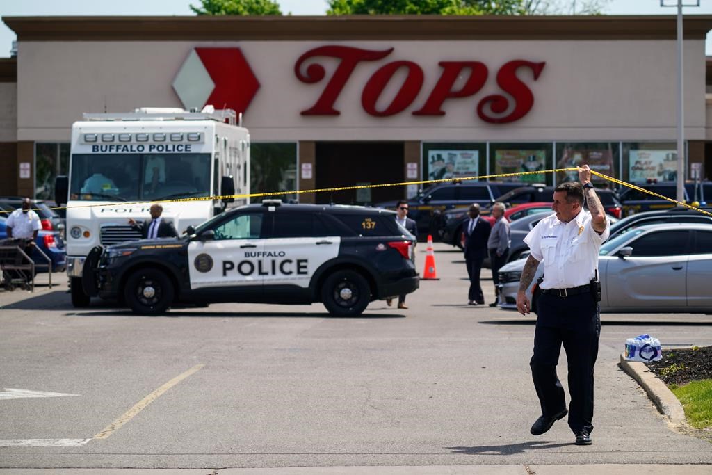 FILE - A police officer lifts the tape cordoning off the scene of a shooting at a supermarket, in Buffalo, N.Y., Sunday, May 15, 2022. Payton Gendron, a white supremacist who killed 10 Black people at a Buffalo supermarket was sentenced to life in prison Wednesday, Feb. 15, 2023 after listening to relatives of his victims express the pain and rage caused by his racist attack. (AP Photo/Matt Rourke, File)