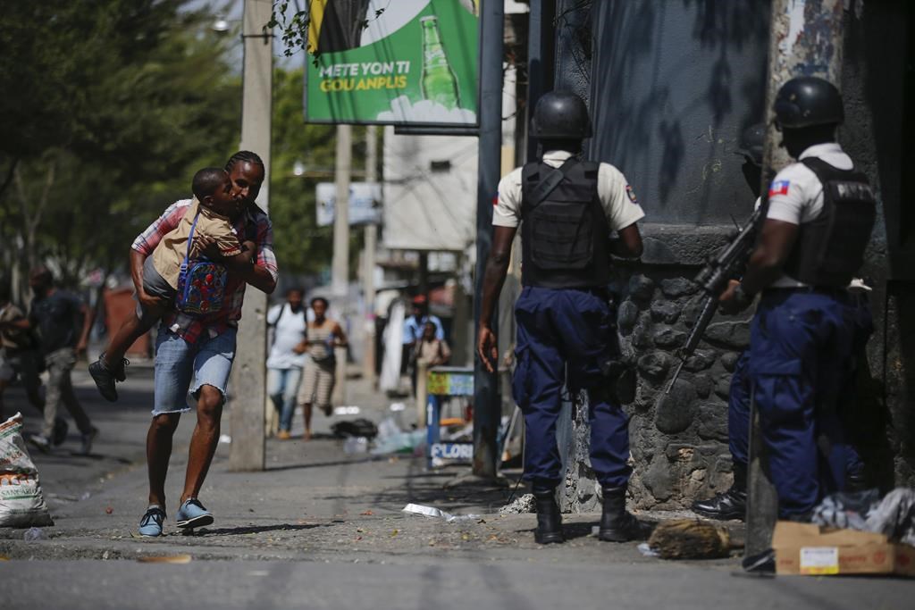 A parent, carrying his child after picking him up from school, runs past police as they carry out an operation against gangs in the Bel-Air area of Port-au-Prince, Haiti, Friday, March 3, 2023. Haiti's troubled government is accusing Ottawa of stalling in its delivery of purchased armoured vehicles, and argues the delay is hindering a plan to clear violent gangs from Port-au-Prince. THE CANADIAN PRESS/AP/Odelyn Joseph