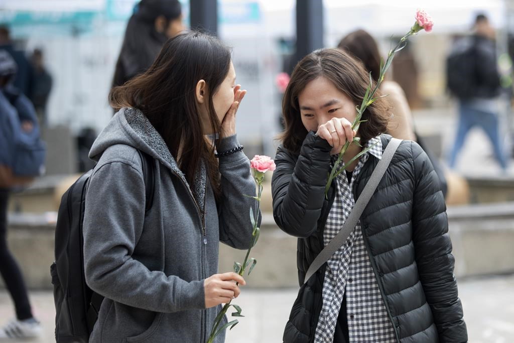 Two women bring flowers as people gather in Toronto's Mel Lastman Square on Tuesday, April 23, 2019 to commemorate a van attack which left 10 people dead. An event commemorating the anniversary of Toronto's attack will be held in the north-end community where the deadly attack took place five years ago today. THE CANADIAN PRESS/Chris Young