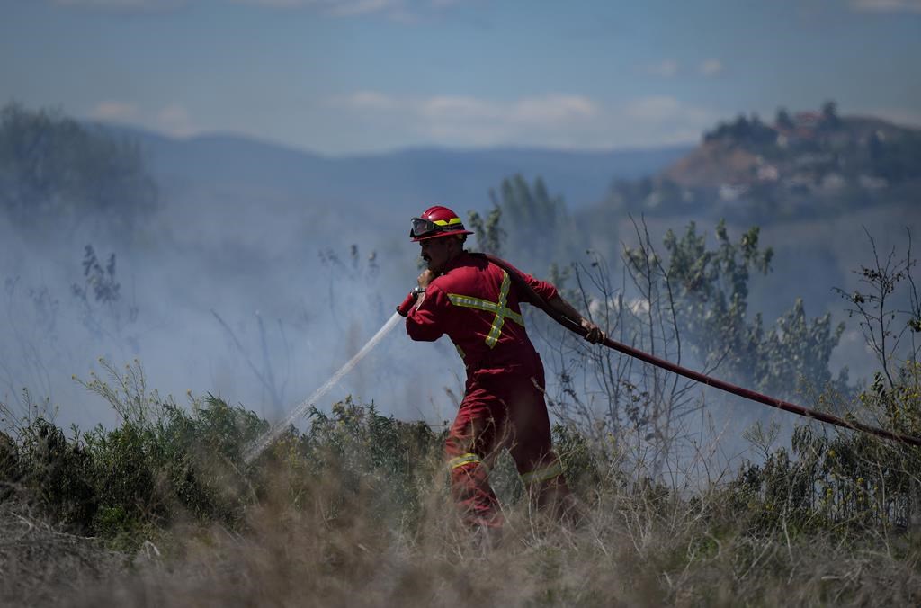 Un pompier dirige de l'eau sur un feu brûlant sur un terrain derrière une propriété résidentielle à Kamloops, en Colombie-Britannique, le lundi 5 juin 2023. 