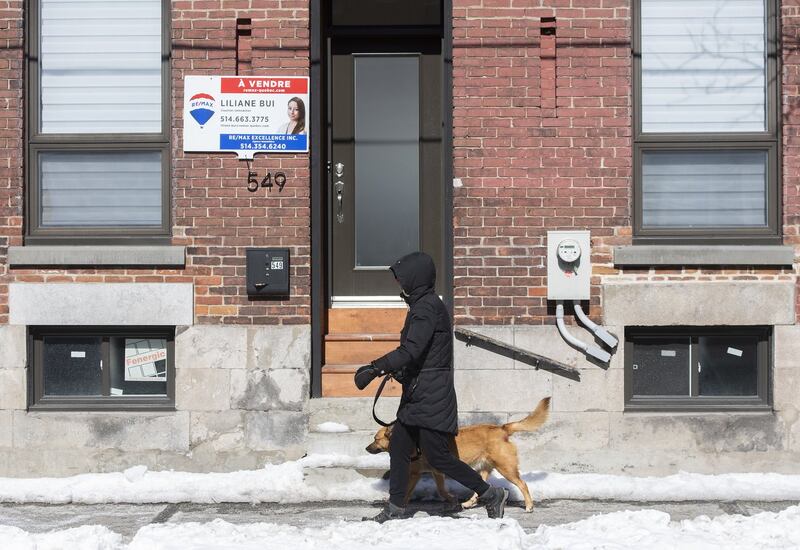 Une femme passe devant une maison à vendre à Montréal, le vendredi 4 mars 2022.