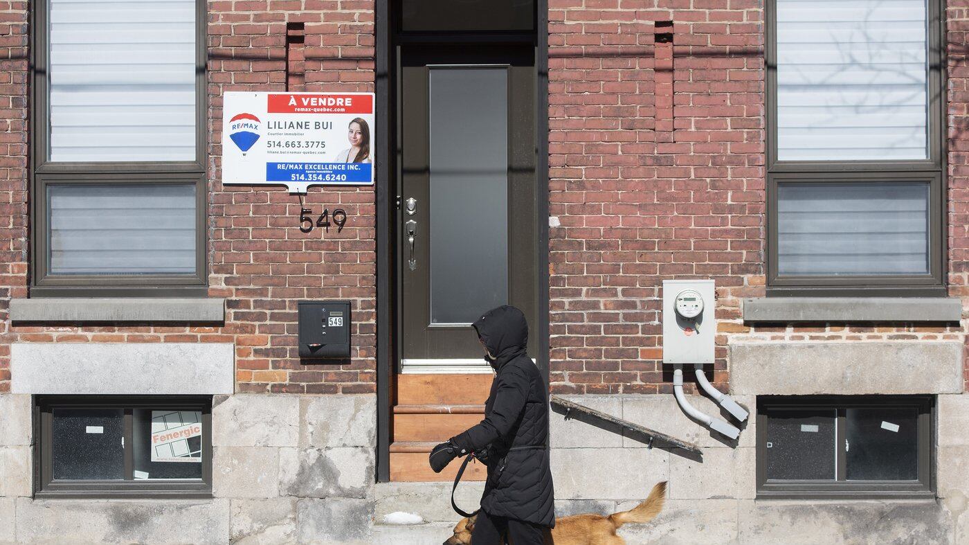 Une femme passe devant une maison à vendre à Montréal, le vendredi 4 mars 2022.