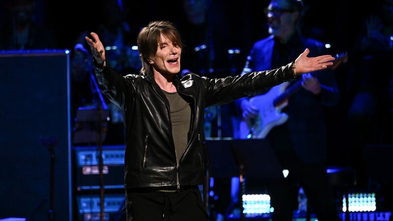 A man is centre stage singing while wearing a black leather jacket.